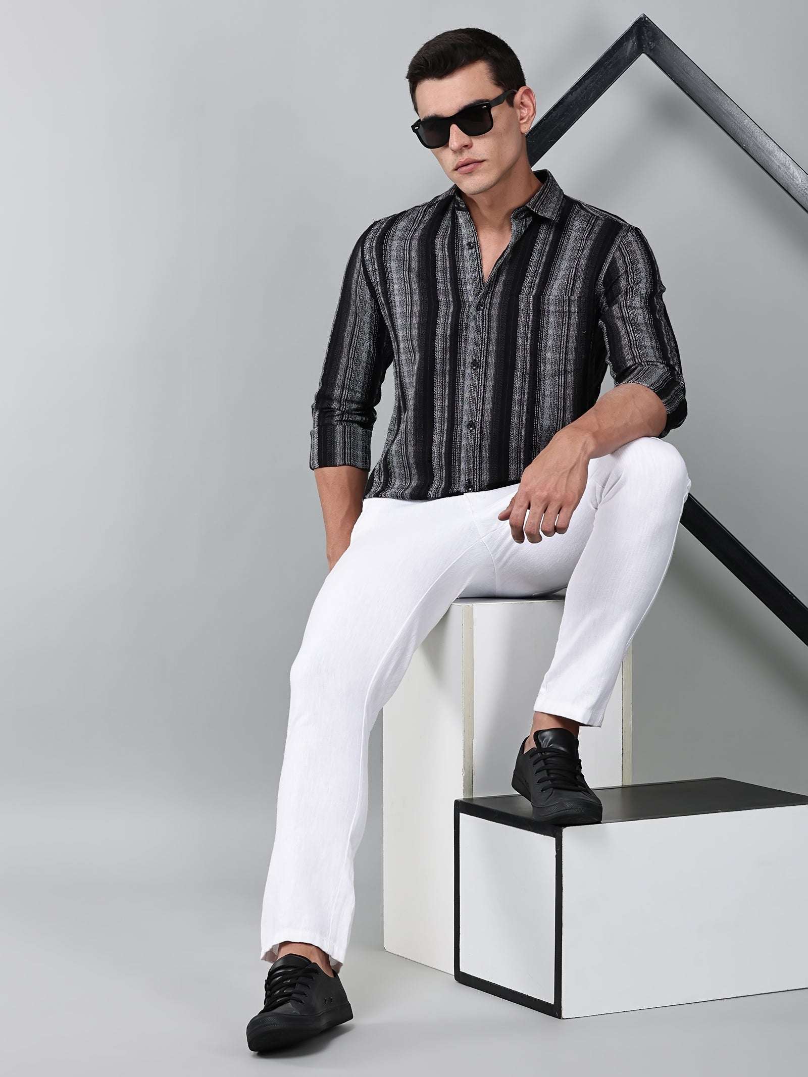 model wearing a noir (black) echo textured stripe shirt with white trousers
