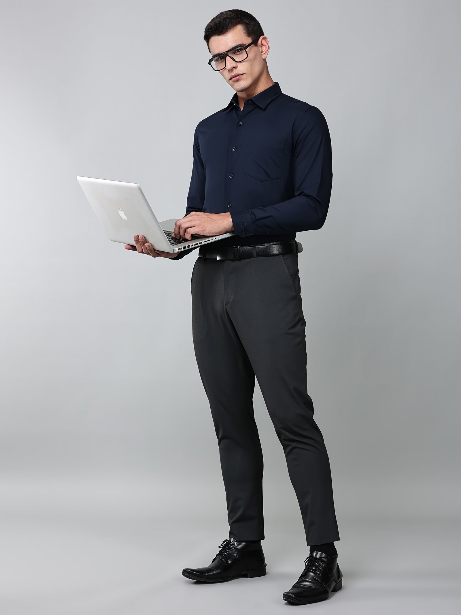 a model wearing a signature textured stretch formal navy blue shirt, grey trousers, black formal shoes, glasses and holding a laptop