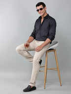 model wearing a luxe satin charcoal grey shirt with beige trousers and black loafers holding a glass in one hand