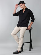 a model wearing a luxe satin black shirt with beige trousers, black loafers and a black hat