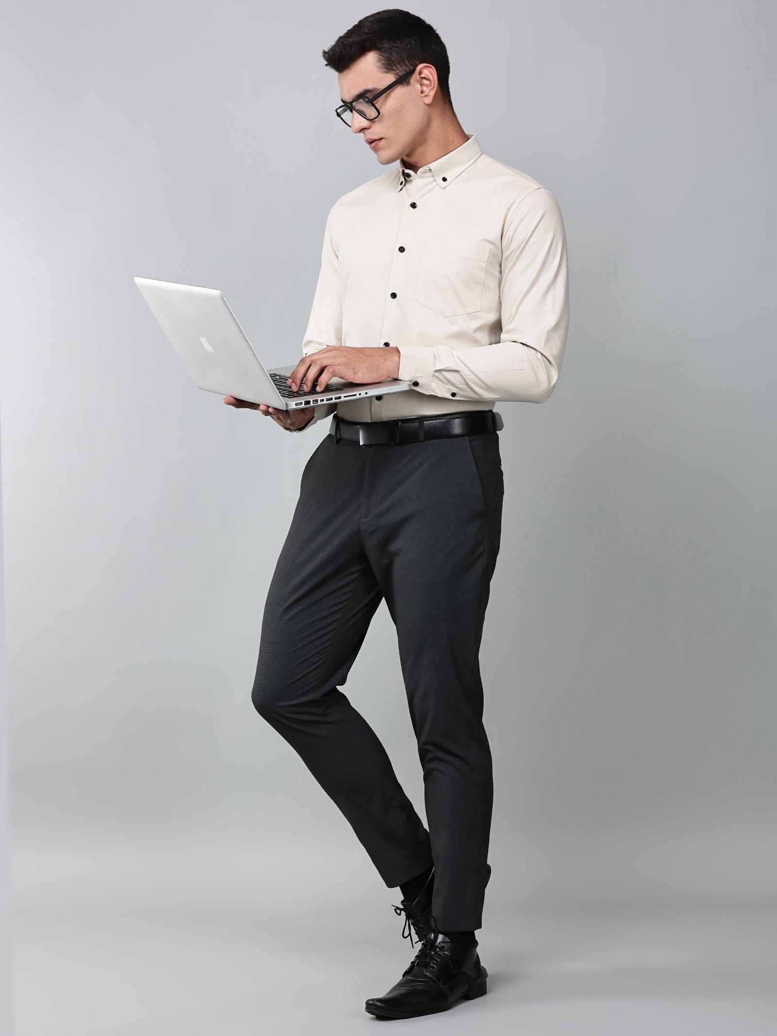 a model wearing a beige heritage linen luxe shirt, dark grey trousers, black formal shoes and a laptop