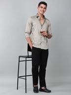 a model wearing a luxe satin ivory stone shirt with black trousers and black loafers and holding a glass in one hand