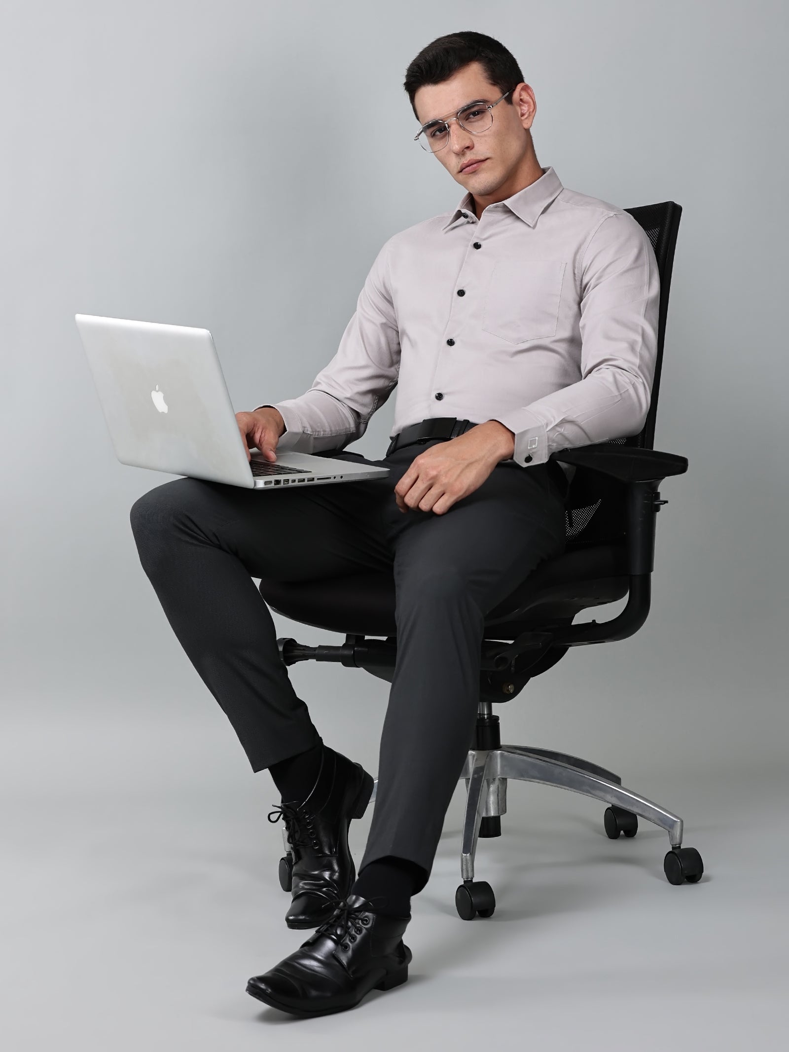 a model wearing a signature textured stretch formal dusk shirt, black trousers, black formal shoes and sitting on a chair with a laptop