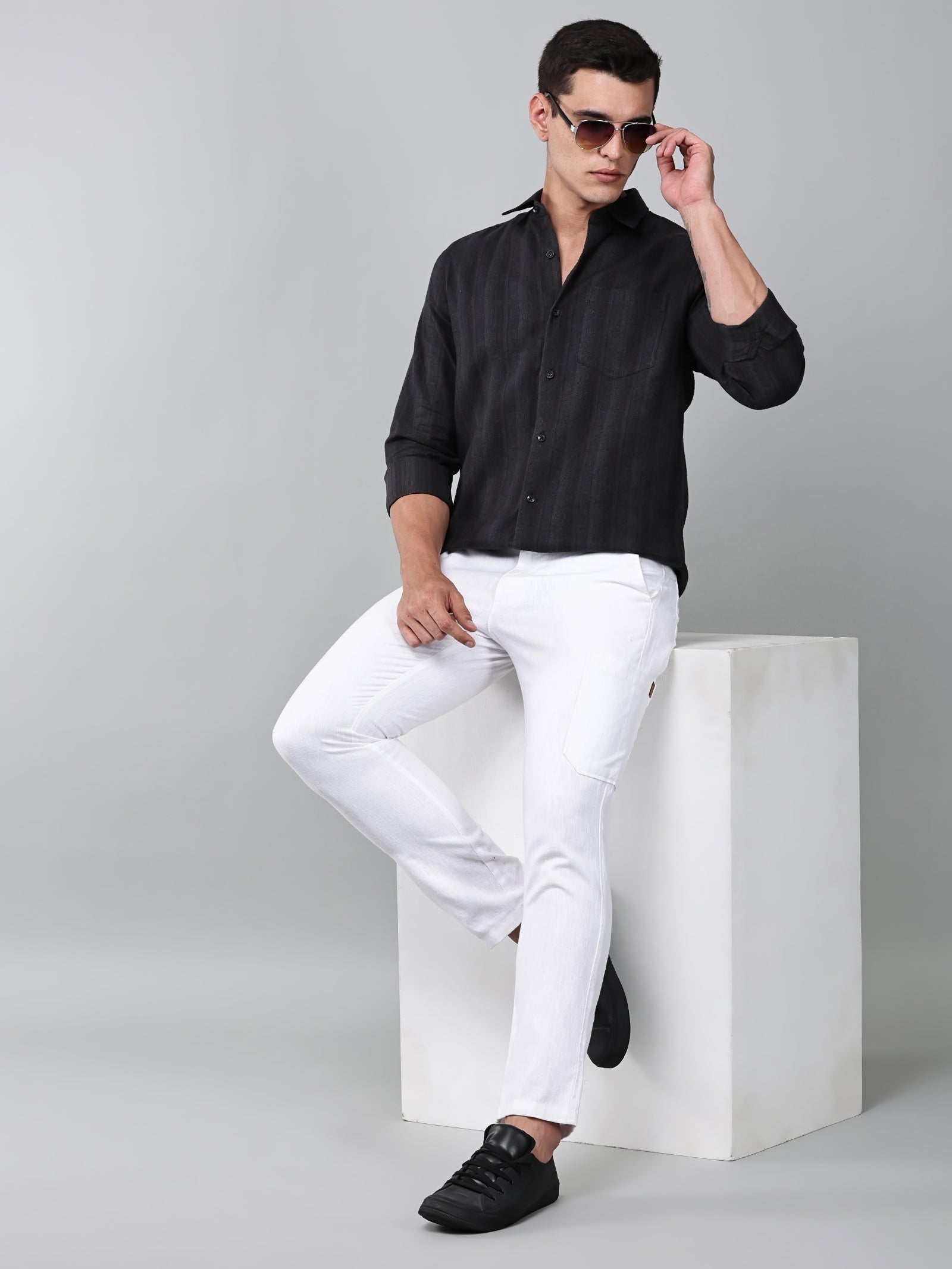 a model wearing a midnight noir (black) obsidian shirt with white trousers and black shoes