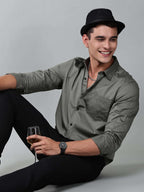 a model wearing a luxe satin olive green shirt with a black hat holding a glass in one hand
